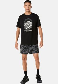 Sort t-shirt med bjergmotiv, kombineret med sorte shorts med bølget mønster. Inkluderer sorte sokker og sportssko.