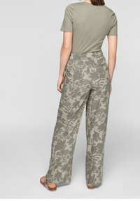 T-shirt en coton vert olive clair associé à un pantalon large taille haute orné d'un motif floral dans des nuances de vert et de beige.