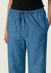 Jeans-joggingbyxor i mellanblått, med elastisk midja och snörning, sidofickor och en avslappnad passform. Slät textur.