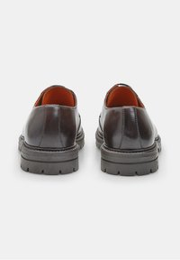 Chaussures en cuir noir avec une surface lisse, dotées d'une épaisse semelle en caoutchouc noir et d'une doublure intérieure orange. L'arrière présente une forme arrondie.