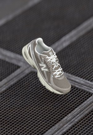 Grå og hvid sportssko med snørebånd svæver over en mørk metalrist overflade.
