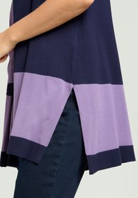 Suéter de punto en tonos azul marino y lavanda con aberturas laterales; presenta un diseño en bloques de color, un ajuste holgado y ribete acanalado en los bordes.