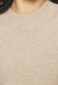 Jasno beżowy sweter dzianinowy z żeberkowym okrągłym dekoltem i gładką teksturą, prezentujący miękki, stonowany wygląd.