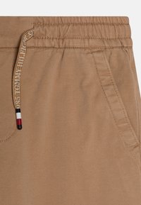 Jasnobeżowe dresy z elastycznym pasem, z troczkiem w czerwono-białe-niebieskie akcenty. Widoczna kieszeń boczna, trwała faktura.