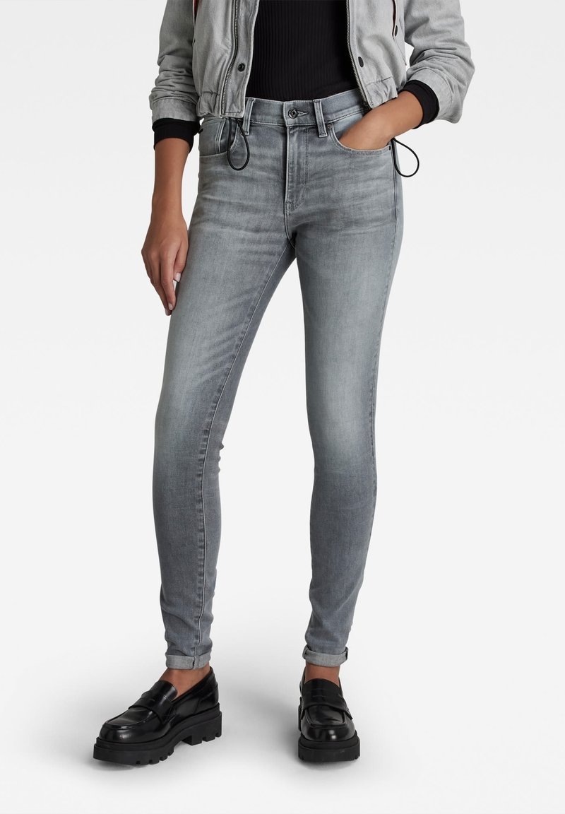 Jeans skinny grises de cintura alta, con una textura desgastada, cierre de cremallera, bolsillos frontales y un corte ajustado hasta el tobillo.