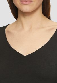Haut noir à col en V fabriqué en tissu doux et côtelé. L'encolure est nette et profonde, mettant en valeur la zone des clavicules.