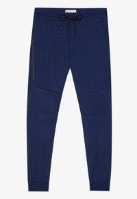Marineblå joggebukser med elastisk liv, snor, sidelommer med glidelås og teksturerte paneldetaljer ved knærne.