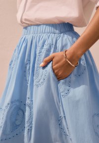 Gonna azzurro chiaro con motivi a cuore ricamati e vita arricciata. Presenta tasche e una texture liscia.
