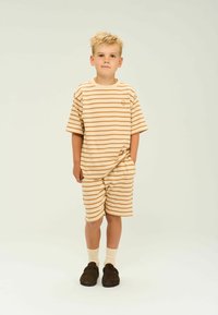 Beige och ljusbrun randig T-shirt och shorts-set. Mjuk textur, lös passform, korta ärmar, med en liten logotyp på t-shirten. Bruna skor.