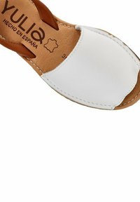 Sandalia de cuero blanco con detalles en marrón, punta abierta y detalles de costura. La plantilla presenta la etiqueta de marca "YULIA, HECHO EN ESPAÑA."