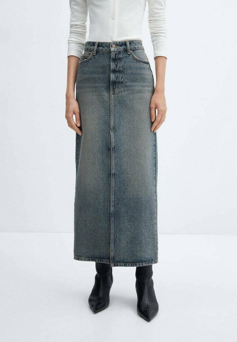 Falda maxi de mezclilla en azul desgastado, con cintura alta, silueta recta, botones frontales y diseño minimalista. Combinada con botas negras de punta.