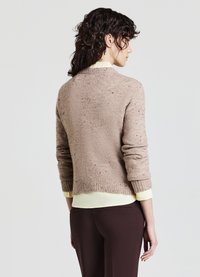 Brauner Strickpullover mit strukturierter Oberfläche, gerippten Bündchen und Saum. Über einem hellgelben Hemd getragen, das einen runden Halsausschnitt und eine cropped Länge aufweist.