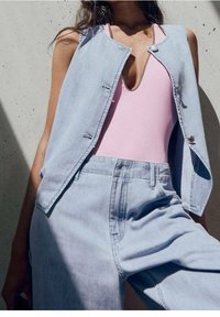 Chaleco de denim de color azul claro, sin mangas y con cierre de botones, combinado con un traje de baño rosa y pantalones a juego de color azul claro.