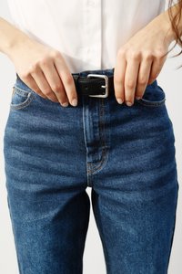 Temno modri kavbojski jeans imajo oprijet kroj s kontrastnim oranžnim šivom. Na pasu je nošen črn usnjen pas z kovinsko zaponko.