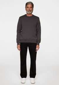 Grå sweatshirt med rund hals, långa ärmar och ribbade muddar, i kombination med svarta byxor och vita sneakers, stående på en neutral bakgrund.