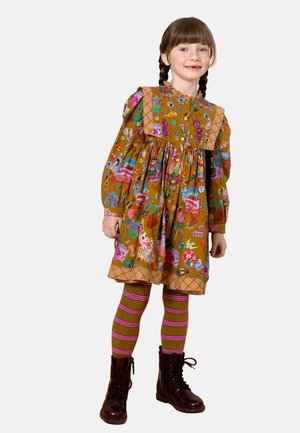 Multikleurige kinderkleed met een uitlopende snit, voorzien van verschillende speelse patronen, een ruches-kraag en een geruit zoom. Gecombineerd met gestreepte legging en bruine laarzen.
