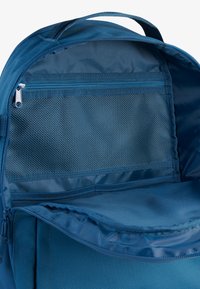 Notranjost modre nahrbtnika z zadrgo, mrežnim predalom in gladko tekstilno površino. Ima ročaj na vrhu in strukturirano zasnovo.