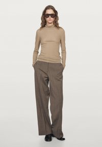 Tan lange mouw turtleneck gecombineerd met bruin gestreepte wijde broek, met een gladde textuur en gedragen met zwarte schoenen.