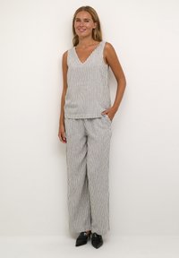 Haut sans manches en v et pantalon large en tissu léger, avec un motif de rayures verticales en noir et blanc. Poches sur le pantalon.