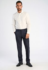 Camicia a maniche lunghe color crema chiaro con colletto classico, pantaloni eleganti neri e scarpe nere. Design aderente, texture liscia e vestibilità su misura.