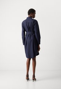 Navyblauwe jurk met lange mouwen, een ceintuur in de taille en een knoopsluiting bij de kraag. Gladde stof met een rugplooi ontwerp.