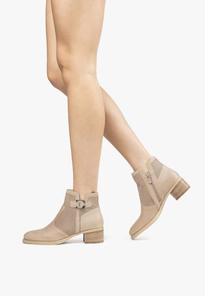 Stivali ankle in pelle beige con design perforato, tacco a blocco basso, zip laterale e dettaglio in metallo. Texture liscia con una forma strutturata.