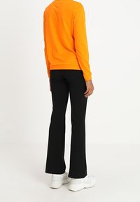 Oranges Langarmshirt kombiniert mit schwarzen Schlaghosen, ergänzt durch weiße Sneakers. Glattes Material mit einem taillierten Schnitt.