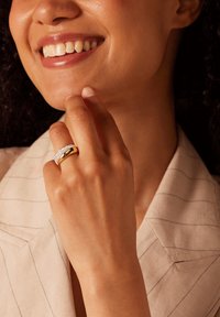 Bague en or avec une accent de diamant, présentant une finition lisse et un design arrondi, portée sur une main de teinte de peau claire.