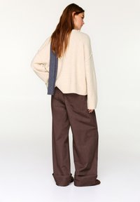 Beżowy sweter z dzianiny o luźnym kroju, z niebieskim paskiem akcentującym. W zestawieniu z luźnymi brązowymi spodniami, prezentujący casualowy styl.