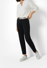 Pantalon noir sur mesure associé à un haut en maille blanc ample, présentant un col en V et des manches mi-longues, complété par des baskets blanches.