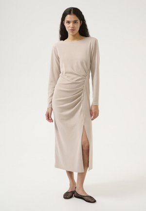 Langärmliges, beiges Kleid mit drapiertem Textur, Seitennaht und Rundhalsausschnitt. Kombiniert mit schwarzen Netz-Ballerinas.
