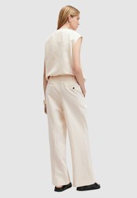 Top senza maniche a strisce beige con una vestibilità rilassata, abbinato a pantaloni larghi a strisce beige. Un paio di semplici scarpe nere slip-on completano l'outfit.