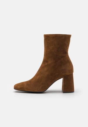 Botas de ante marrones hasta el tobillo con tacón cuadrado, punta afilada, textura suave y diseño minimalista.