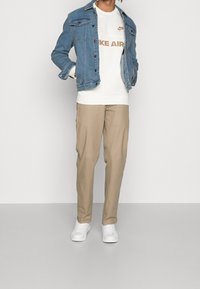 Denimjacka i ljusblått, vit sweatshirt med texten "Nike Air", beige byxor och vita sneakers. Har en klassisk design och avslappnad passform.