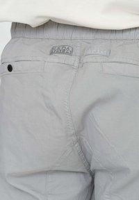 Pantaloni grigi chiari con vita elastica, caratterizzati da tessuto strutturato, una tasca posteriore e etichette di marca cucite in vita.