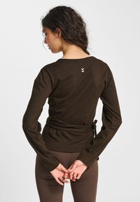 Bruine lange mouwen wikkeltop met een gestructureerde afwerking, voorzien van een strik in de taille en een klein logo-detail op de achterkant van de halslijn.