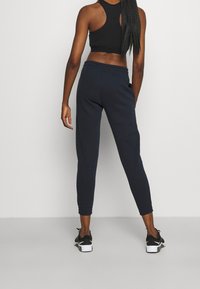 Svart kort topp och marinblå joggers, figursydd design, elastisk midjeband, ribbad struktur, kombinerat med svarta sportskor med vita detaljer.