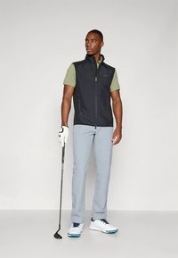 Golfo apranga, kurioje yra juoda be rankovių liemenė, žalia polo marškinėliai, �šviesiai pilkos kelnės ir balti batai su mėlynomis detalėmis. Taip pat yra golfo lazda.