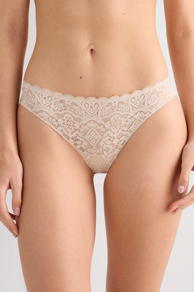 Mujer con ropa interior tipo bikini de encaje color nude con patrones florales y geométricos, mostrada desde la cintura hasta la mitad del muslo.