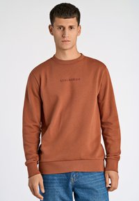 Felpa marrone con colletto a girocollo, maniche lunghe e polsini a coste. La parte anteriore presenta un ricamo "LINDBERGH" in una tonalità più scura.