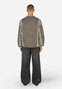 Sivý pruhovaný pletený sveter s uvoľneným strihom a širokými rukávmi, skombinovaný s voľnými tmavosivými džínsami s viditeľnými vreckami.