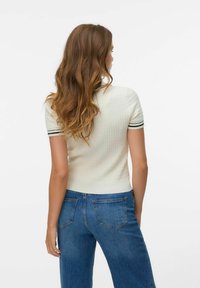 Top a maniche corte in maglia a costine bianco sporco con dettagli a strisce nere sulle maniche. Abbinato a jeans di jeans blu con tasche posteriori.