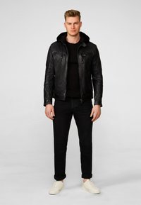 Zwarte leren jack met een capuchon, rits aan de voorkant en borstzakken. Draagt over een zwart T-shirt en gecombineerd met donkere jeans en witte sneakers.