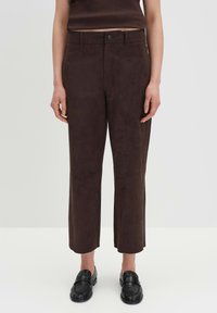 Braune Wildleder-Cropped-Hosen mit geradem Bein, ausgestattet mit einem vorderen Knopfverschluss und einer glatten, weichen Textur. Kombiniert mit schwarzen Schuhen.