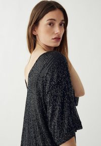 Top negru cu mâneci scurte, lejere, prezentând un model texturat de paiete dispuse pe verticale. Decolteul adânc la spate adaugă un detaliu de design.