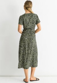 Green, short-sleeve midi dress with a black and white leopard print, featuring a cinched waist and flowing fabric, paired with black sandals.
