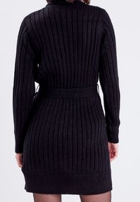 Robe noire tricotée avec un motif à côtes verticales, des manches longues et une ceinture assortie à la taille, avec un col rond et une longueur mi-cuisse.