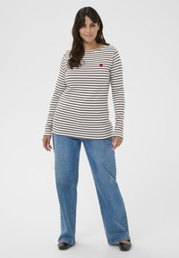 Langærmet stribet skjorte i cremet og mørkebrun, med en lille rød hjertebrodering, parret med brede blå jeans.