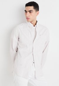 Light-colored button-up shirt with thin vertical stripes, long sleeves, and a chest pocket, worn over a plain white t-shirt.