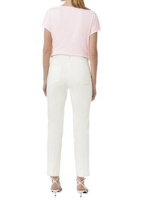 Lichtroze top met korte mouwen gecombineerd met witte op maat gemaakte broeken, met een soepele textuur en achterzakken. Lage hakken met gekruiste sandalen.